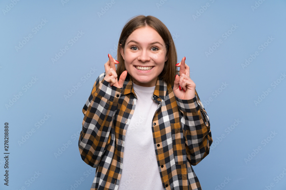 Young woman over blue wall with fingers crossing Young woman over blue wall with fingers crossing