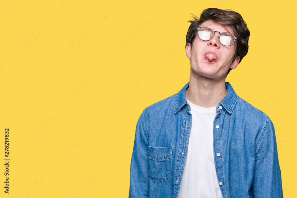 Fototapeta premium Young handsome man wearing glasses over isolated background sticking tongue out happy with funny expression. Emotion concept.
