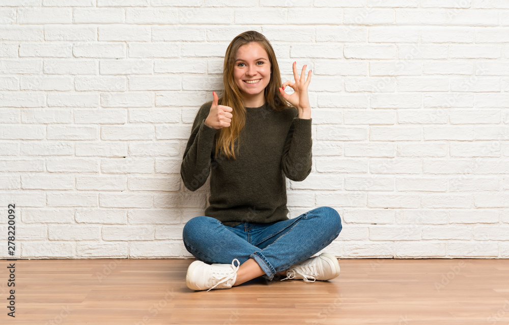 Young woman sitting on the floor showing ok sign and thumb up gesture Young woman sitting on the floor showing ok sign and thumb up gesture