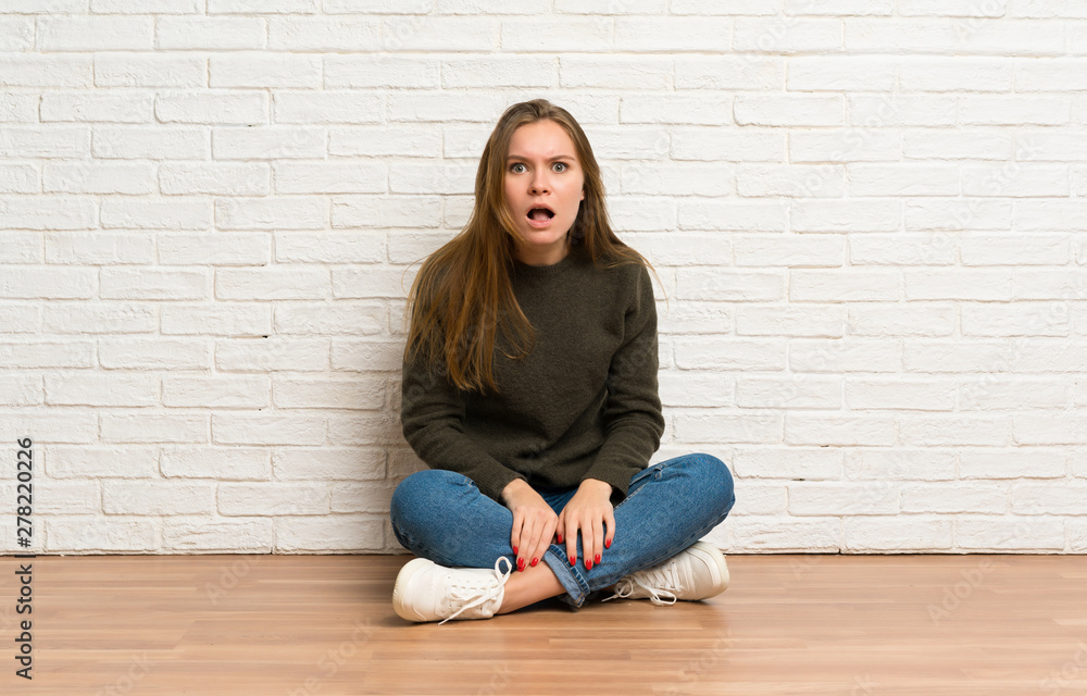 Young woman sitting on the floor with surprise facial expression Young woman sitting on the floor with surprise facial expression