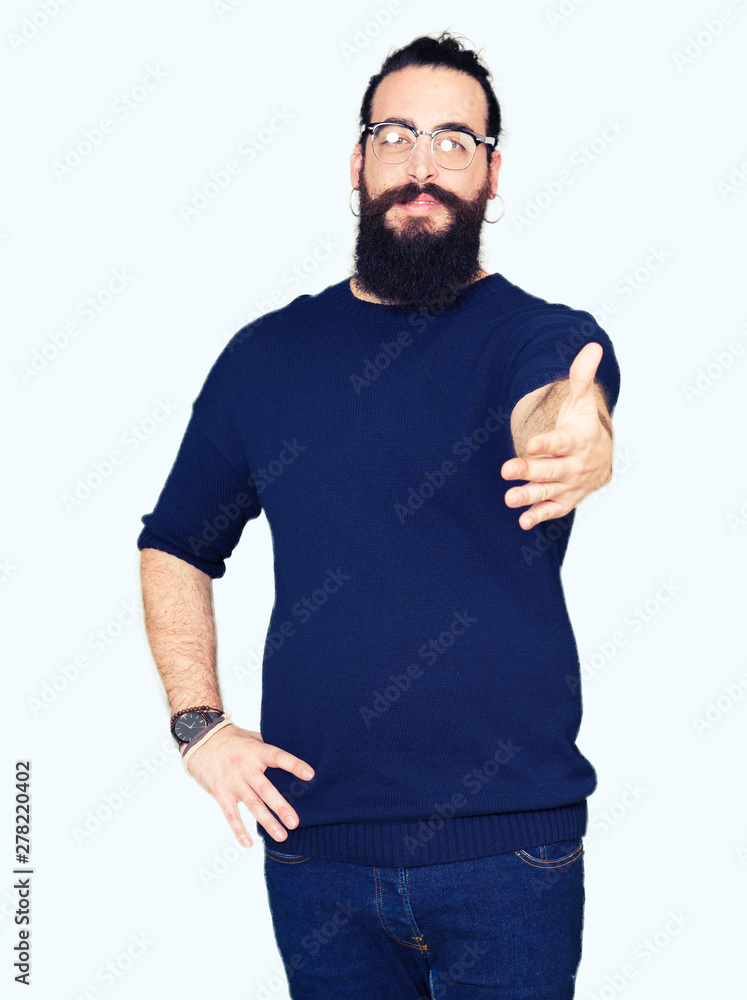 Young hipster man with long hair and beard wearing glasses smiling friendly offering handshake as greeting and welcoming. Successful business. Young hipster man with long hair and beard wearing glasses smiling friendly offering handshake as greeting and welcoming. Successful business.