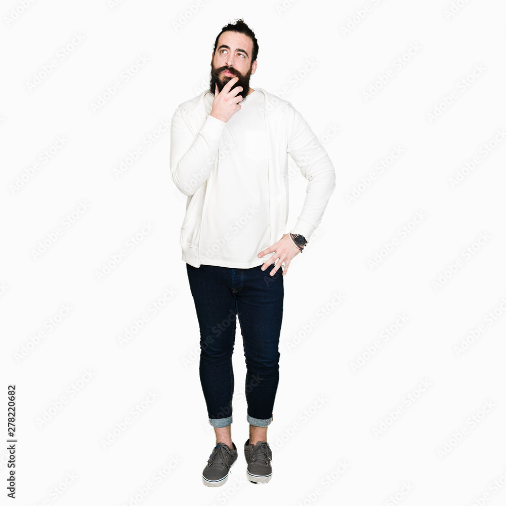 Young man with long hair and beard wearing sporty sweatshirt with hand on chin thinking about question, pensive expression. Smiling with thoughtful face. Doubt concept. Young man with long hair and beard wearing sporty sweatshirt with hand on chin thinking about question, pensive expression. Smiling with thoughtful face. Doubt concept.