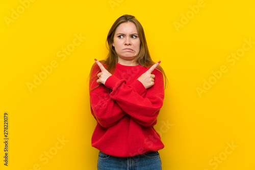 Young woman over yellow wall pointing to the laterals having doubts