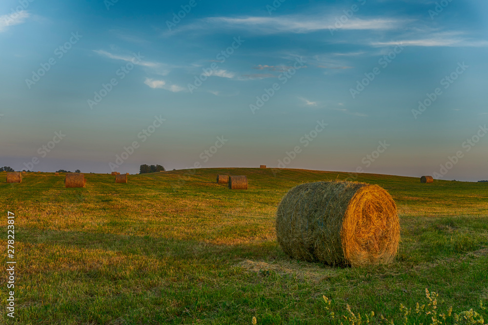 Large round hay bale on a farm field at sunset