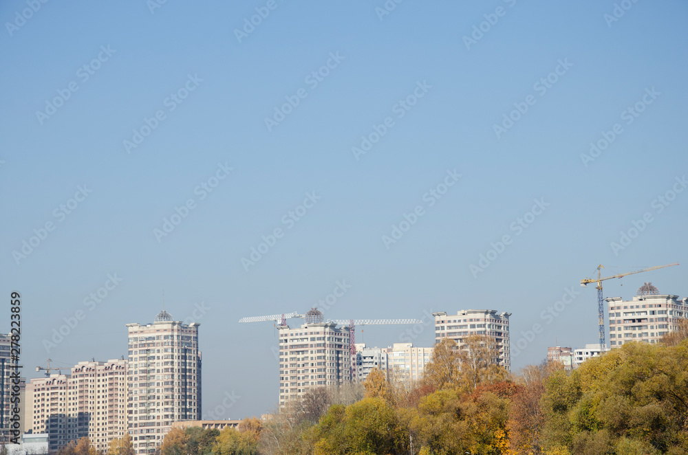  High-rise residential buildings and construction cranes on blue sky background. City in autumn