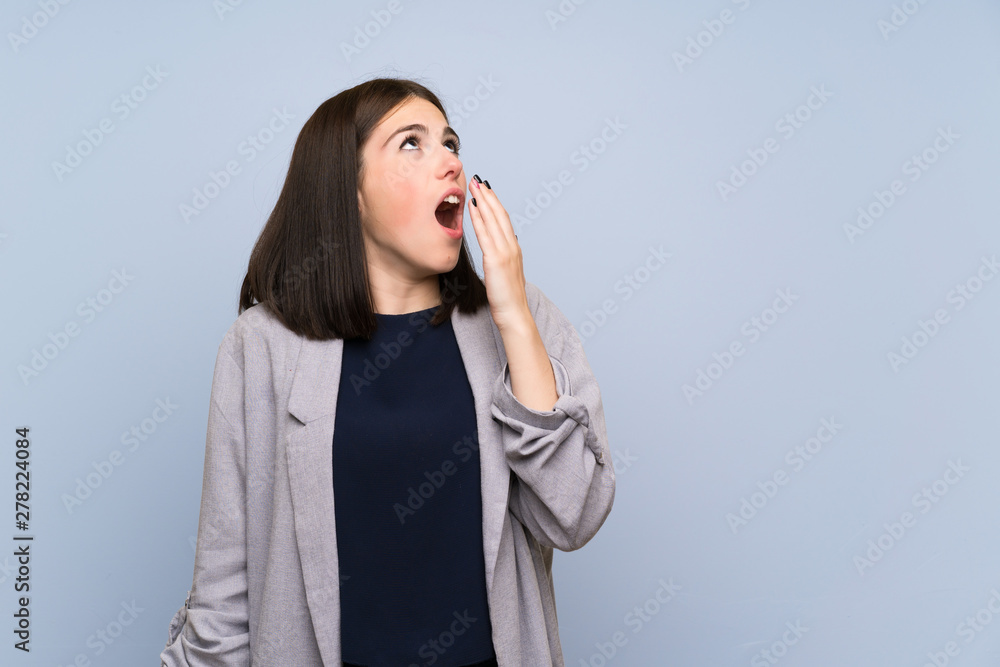 Young woman over isolated blue wall yawning and covering wide open mouth with hand Young woman over isolated blue wall yawning and covering wide open mouth with hand