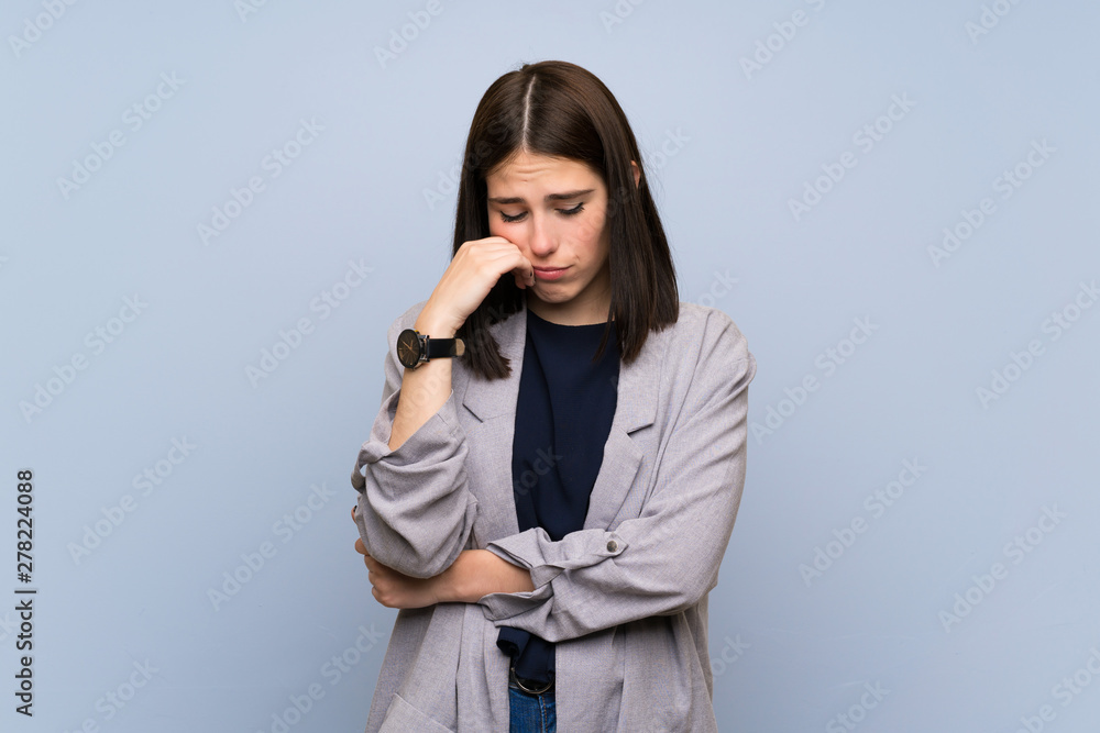 Young woman over isolated blue wall with sad and depressed expression
