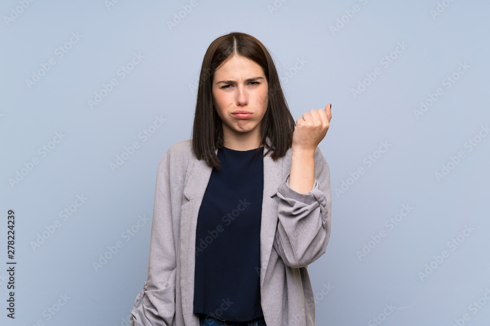 Young woman over isolated blue wall with angry gesture Young woman over isolated blue wall with angry gesture