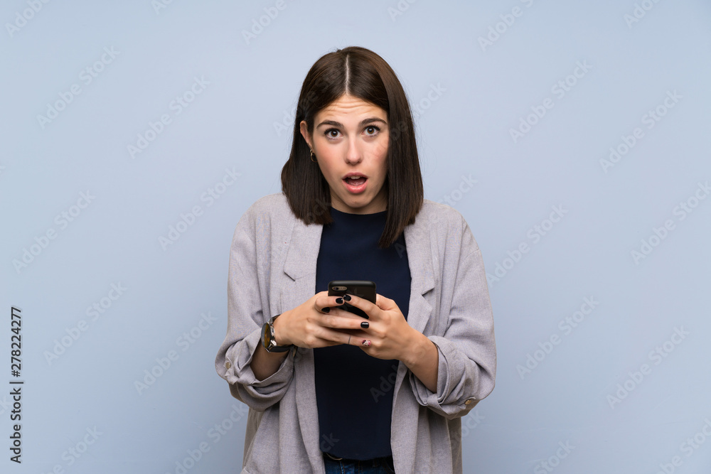 Young woman over isolated blue wall surprised and sending a message Young woman over isolated blue wall surprised and sending a message