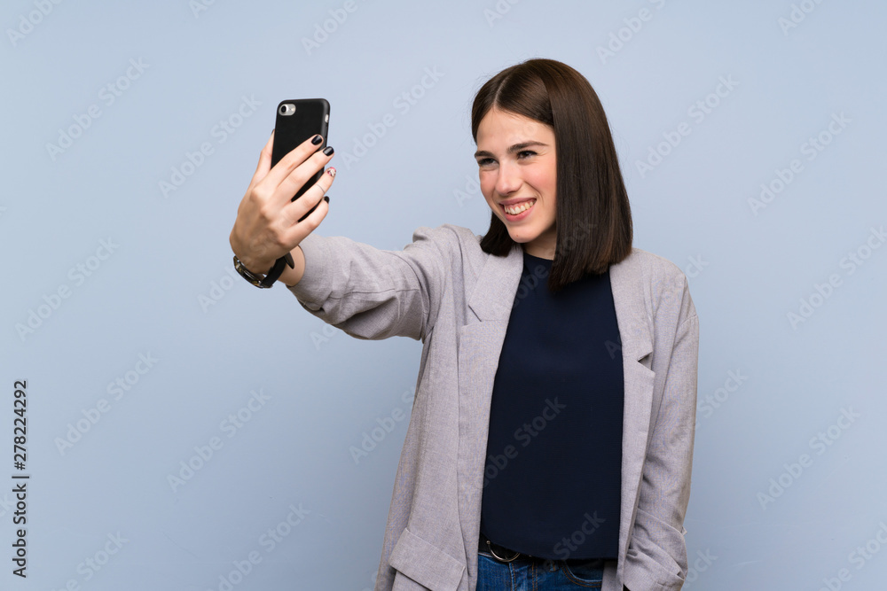 Young woman over isolated blue wall making a selfie Young woman over isolated blue wall making a selfie