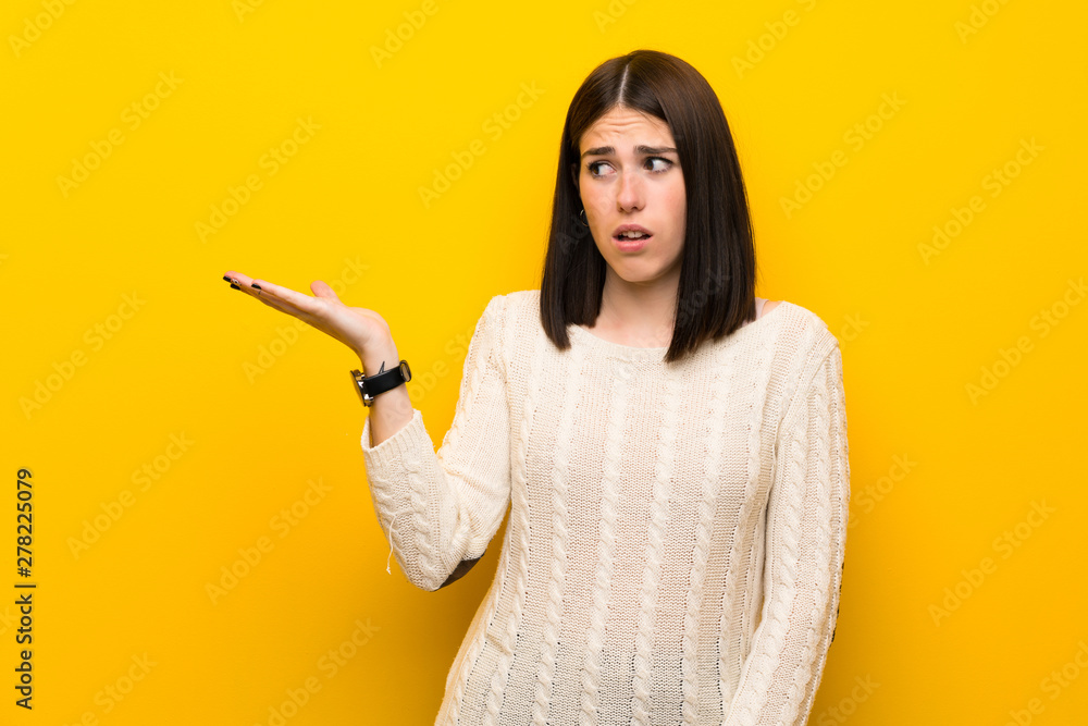 Young woman over isolated yellow wall making doubts gesture Young woman over isolated yellow wall making doubts gesture
