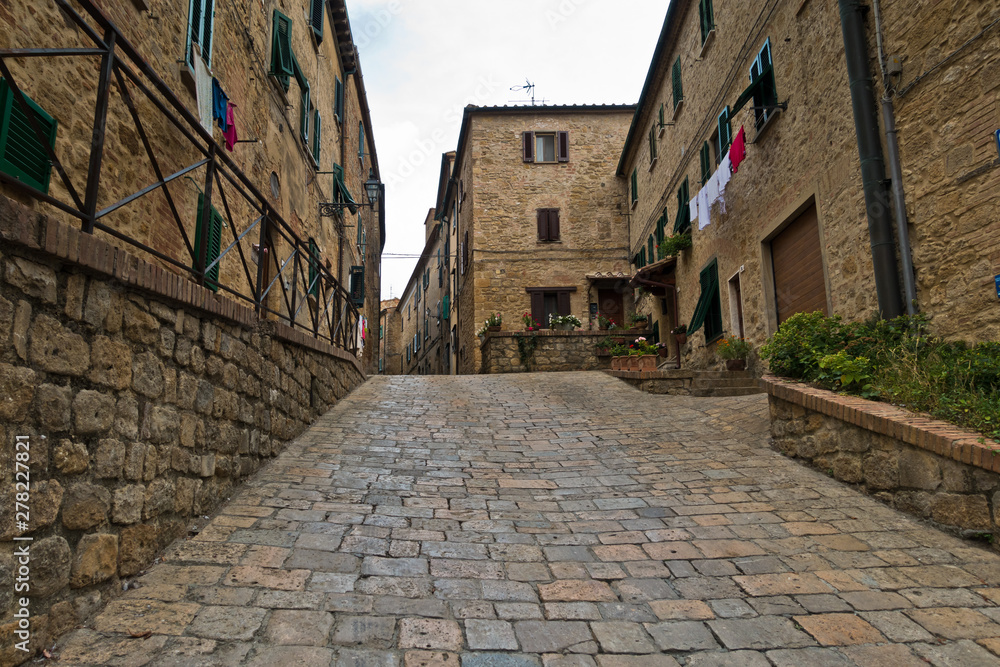 Steep cobblestone street surrounded by vintage stone buildings in Voltera, Tuscany, Italy