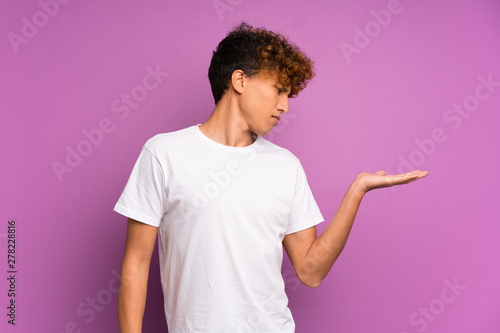 Young african american man over isolated purple wall holding copyspace with doubts