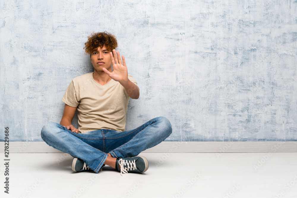 Young african american man sitting on the floor making stop gesture