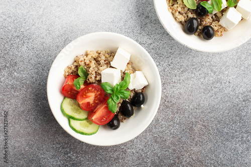 Healthy balanced appetizing salad bowl with quinoa, cucumber, tomatoes, feta cheese, olives, basil leaves on a gray background in a white plate photo