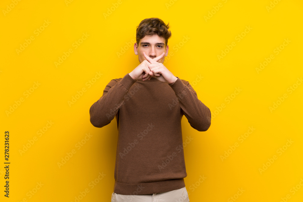 Handsome young man over isolated yellow background showing a sign of silence gesture Handsome young man over isolated yellow background showing a sign of silence gesture