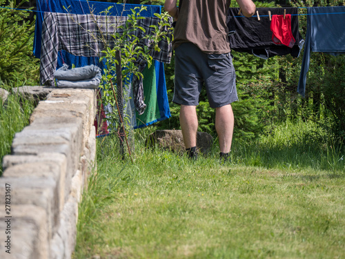 Young man hanging up laundry on a garden clothesline, sandstone wall, copy space photo