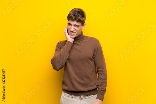 Handsome young man over isolated yellow background with toothache
