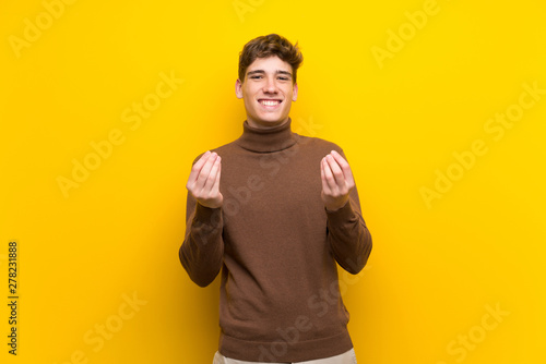 Handsome young man over isolated yellow background making money gesture