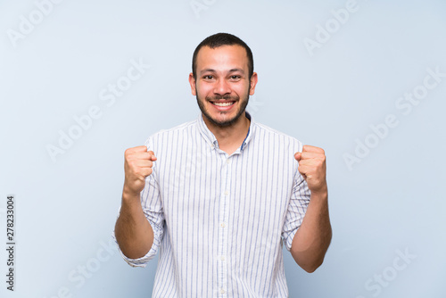 Colombian man over isolated blue wall celebrating a victory in winner position