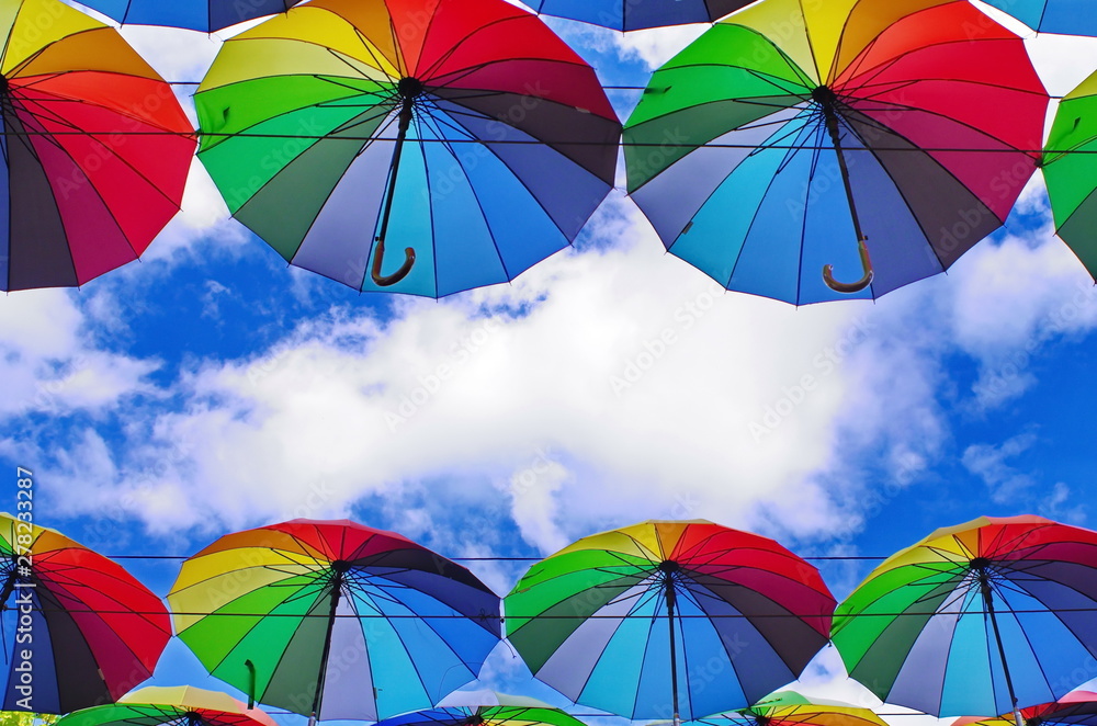 colorful rainbow bright umbrellas  street decoration against a blue sky with fluffy clouds