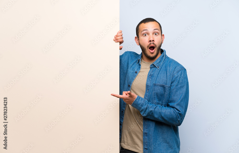 Colombian man holding an empty placard surprised and pointing finger to the side Colombian man holding an empty placard surprised and pointing finger to the side