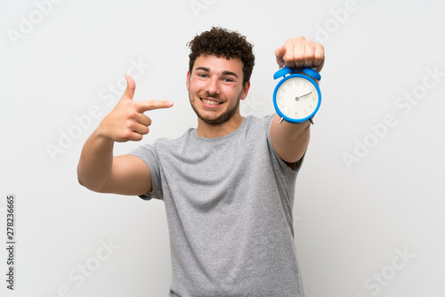 Man with curly hair over isolated wall holding vintage alarm clock