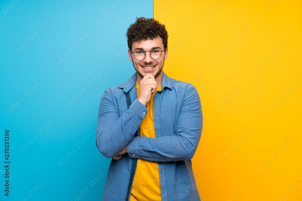 Fototapeta premium Man with curly hair over colorful wall with glasses and smiling