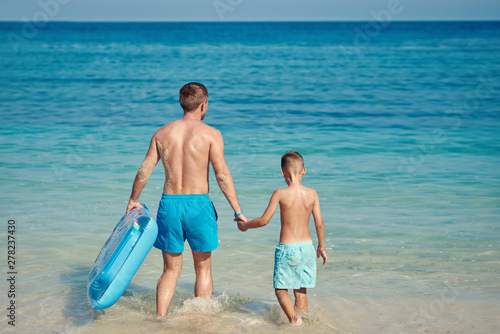 Dad and son with inflatable mattress on the beach.