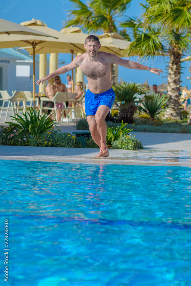 Guy running to jump into swimming pool water at resort.