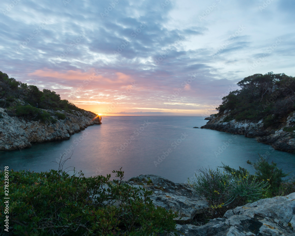 Sunrise from a small bay with orange and yellow sky in Mallorca, Spain. 