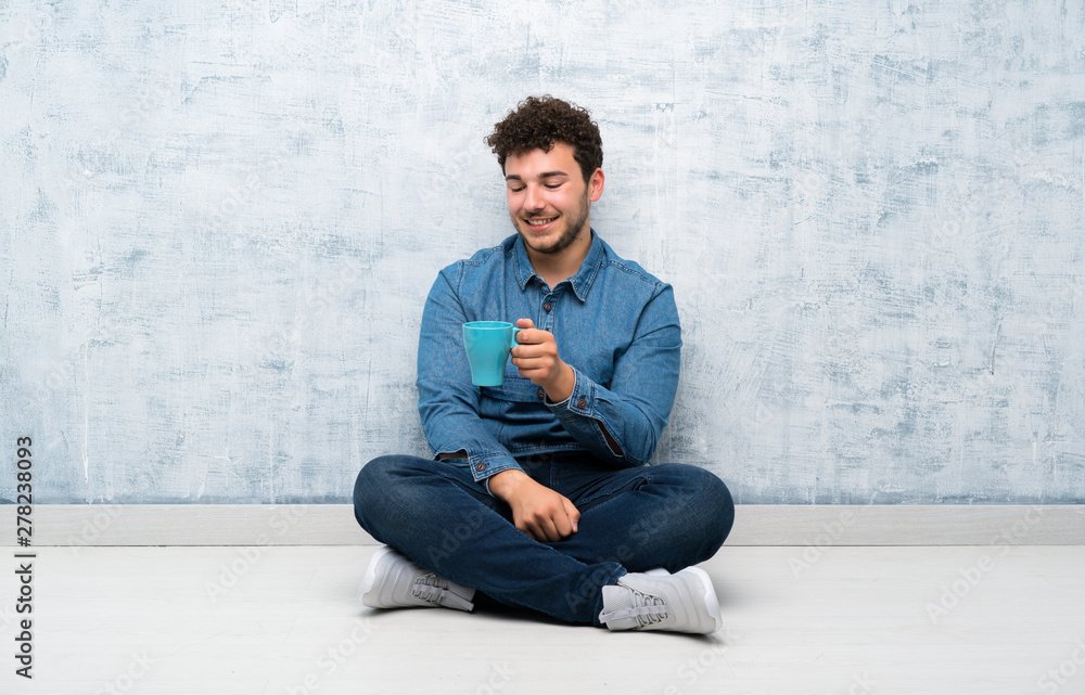Young man sitting on the floor holding hot cup of coffee Young man sitting on the floor holding hot cup of coffee