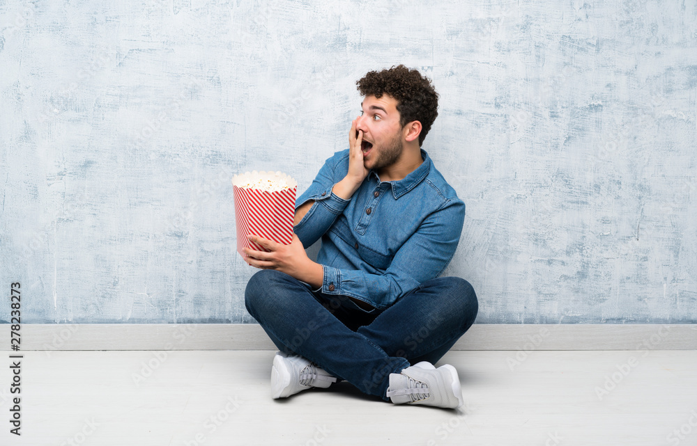 Young man sitting on the floor holding a bowl of popcorns Young man sitting on the floor holding a bowl of popcorns