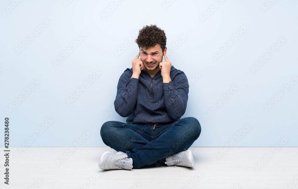 Young man sitting on the floor frustrated and covering ears Young man sitting on the floor frustrated and covering ears