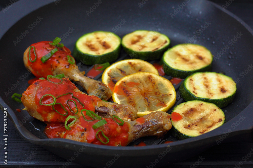 grilled chicken, tomato sauce and zucchini on a griddle, black background grilled chicken, tomato sauce and zucchini on a griddle, black background