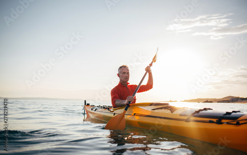 Senior man paddling kayak on the sunset sea