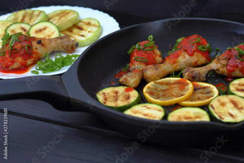 grilled chicken, tomato sauce and zucchini on a plate, black background