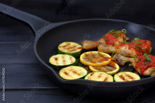 grilled chicken, tomato sauce and zucchini on a griddle, black background