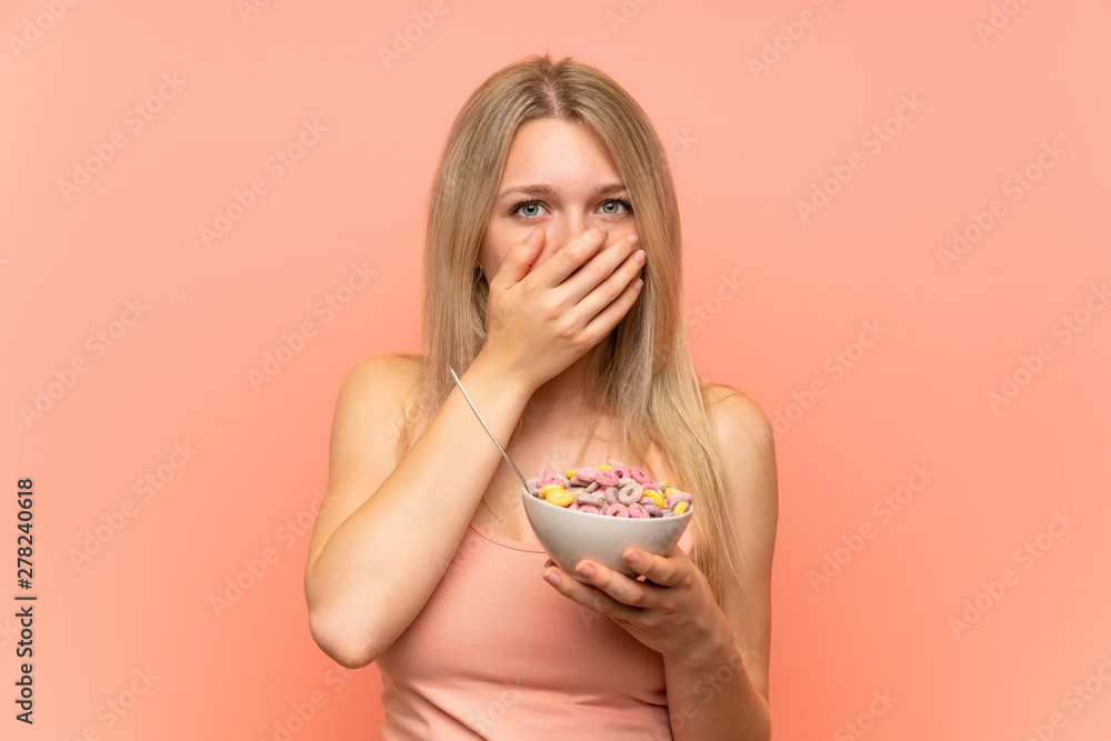 Young woman with popcorns over pink wall covering mouth with hands Young woman with popcorns over pink wall covering mouth with hands