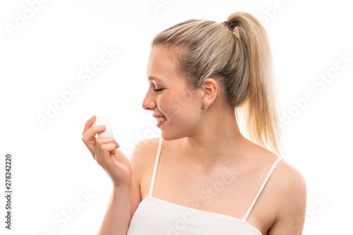 Young blonde woman over isolated white background with moisturizer