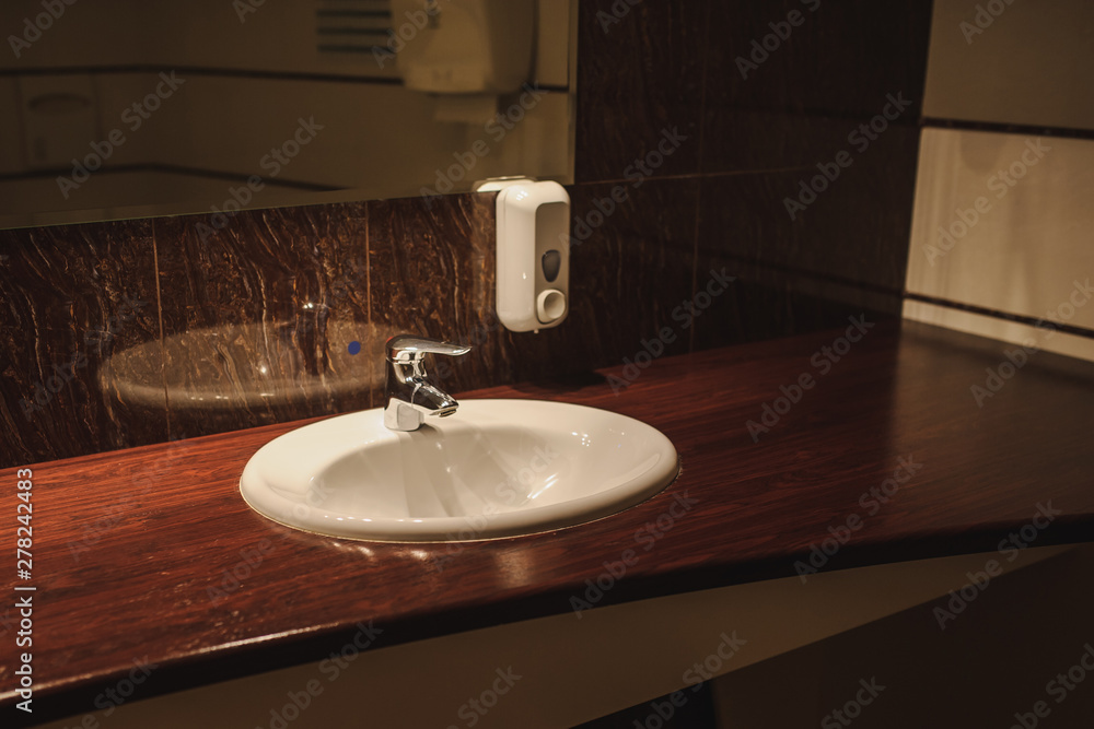Fototapeta premium close up photo of a white oval sink and a steel faucet on a brown wooden table in the bathroom of a spa centre