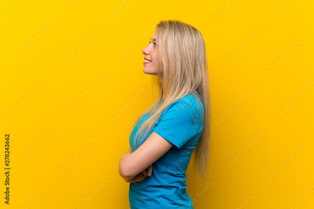 Young blonde woman over isolated yellow background in lateral position Young blonde woman over isolated yellow background in lateral position