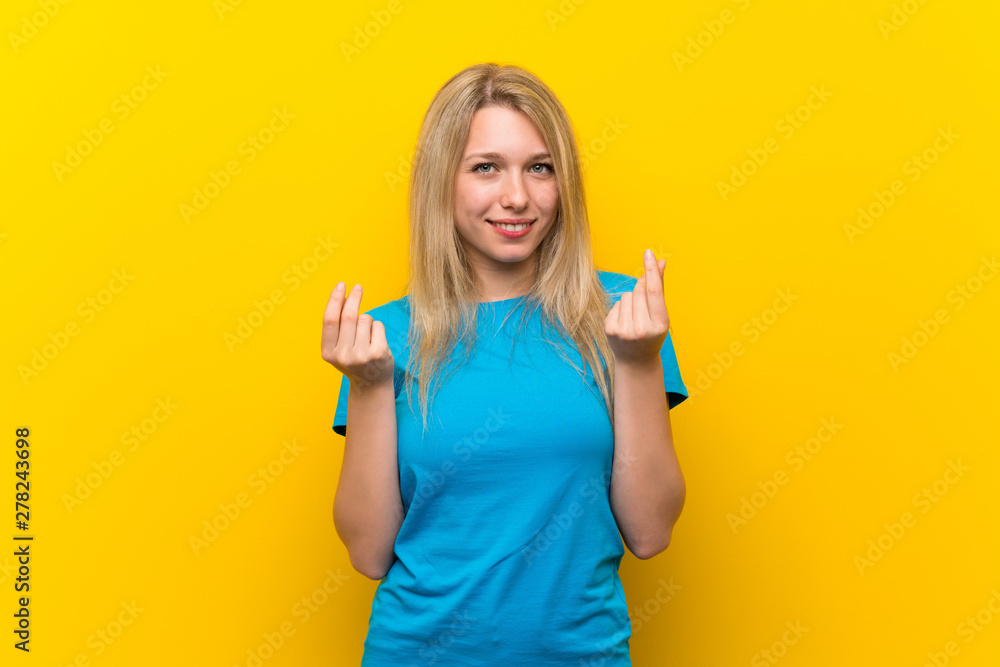 Young blonde woman over isolated yellow background making money gesture Young blonde woman over isolated yellow background making money gesture