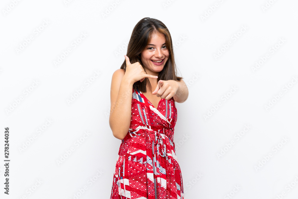 Caucasian girl in red dress over isolated white wall making phone gesture and pointing front Caucasian girl in red dress over isolated white wall making phone gesture and pointing front