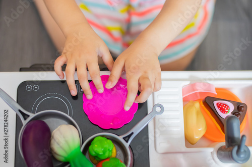 Little girl chef cooking in toy kitchen. Kids play and cook at home or daycare. Toddler kid playing with toy vegetables and dishes.