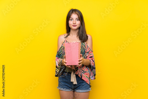 Caucasian girl in colorful dress over isolated yellow background holding a bowl of popcorns