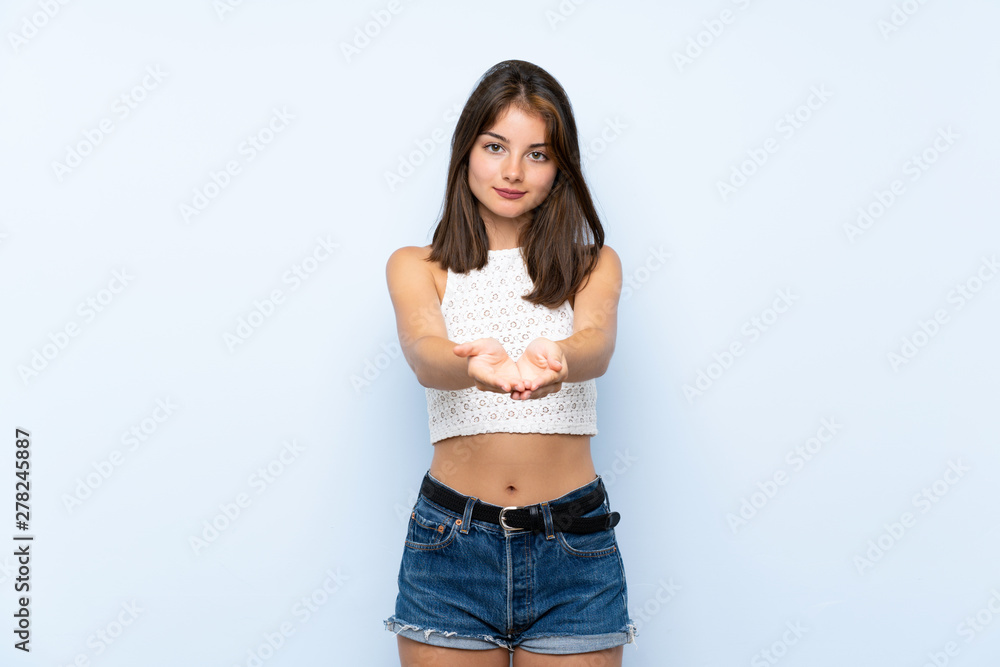 Young woman over isolated blue background holding copyspace imaginary on the palm to insert an ad Young woman over isolated blue background holding copyspace imaginary on the palm to insert an ad