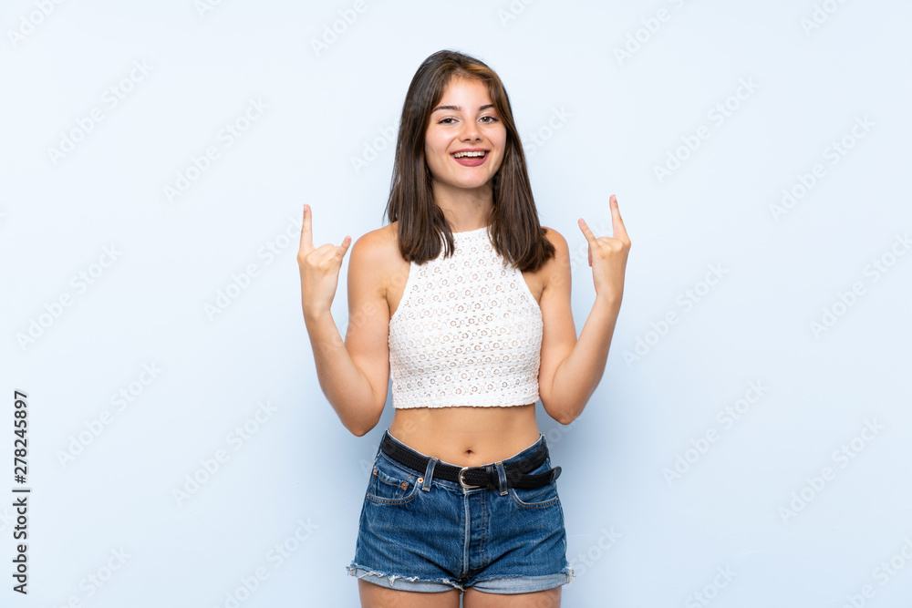 Young woman over isolated blue background making rock gesture Young woman over isolated blue background making rock gesture