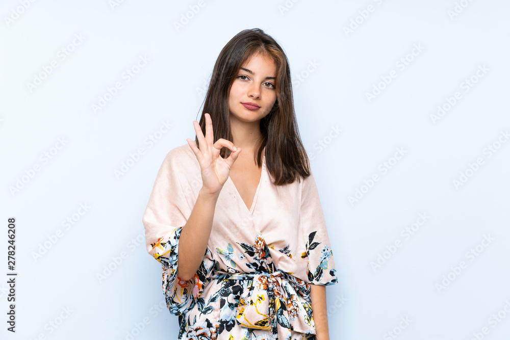 Caucasian girl with kimono over isolated blue background showing an ok sign with fingers Caucasian girl with kimono over isolated blue background showing an ok sign with fingers