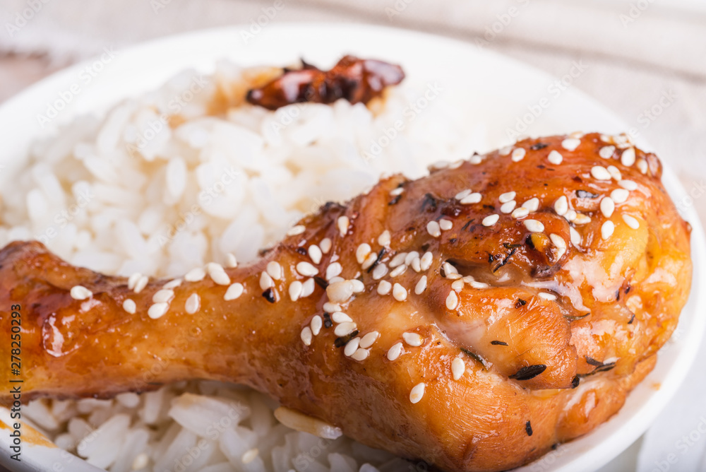 Bowl of rice and chicken drumstick fried in a sticky sweet sauce, sprinkled with sesame, close-up, Asian cuisine